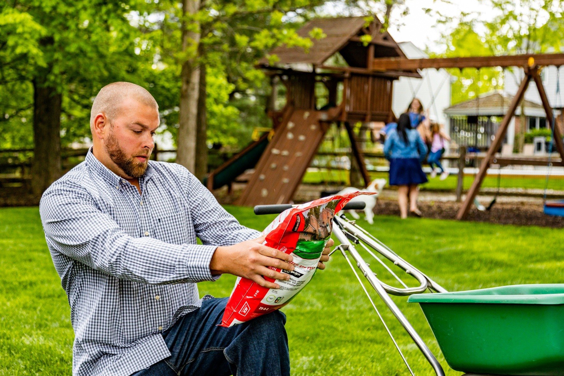 customer reads fertilization bag while family plays in backyard