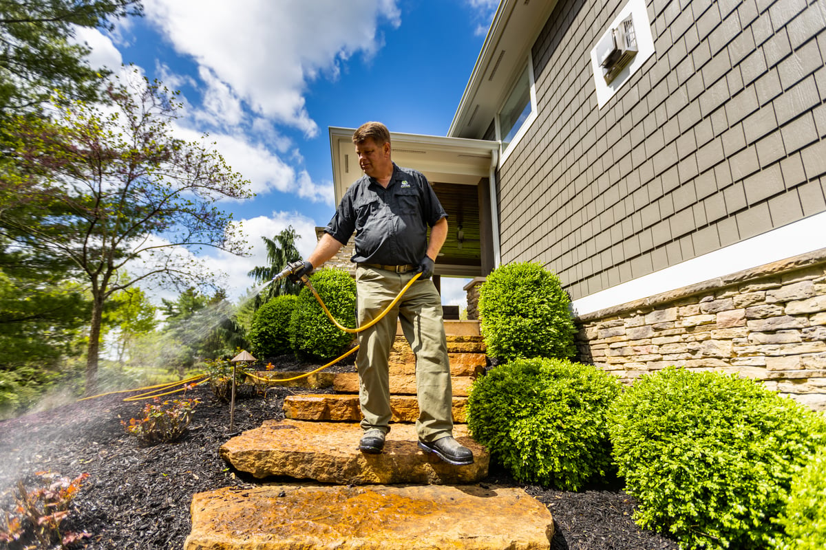 pest control technician spraying landscape bed for mosquitoes
