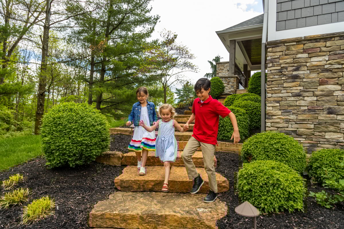 children go down stone steps at home with tidy landscaping