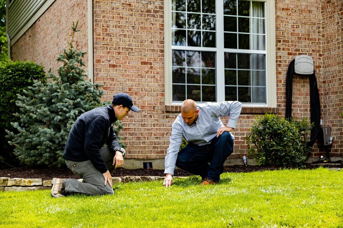 lawn care technician inspects grass with homeowner