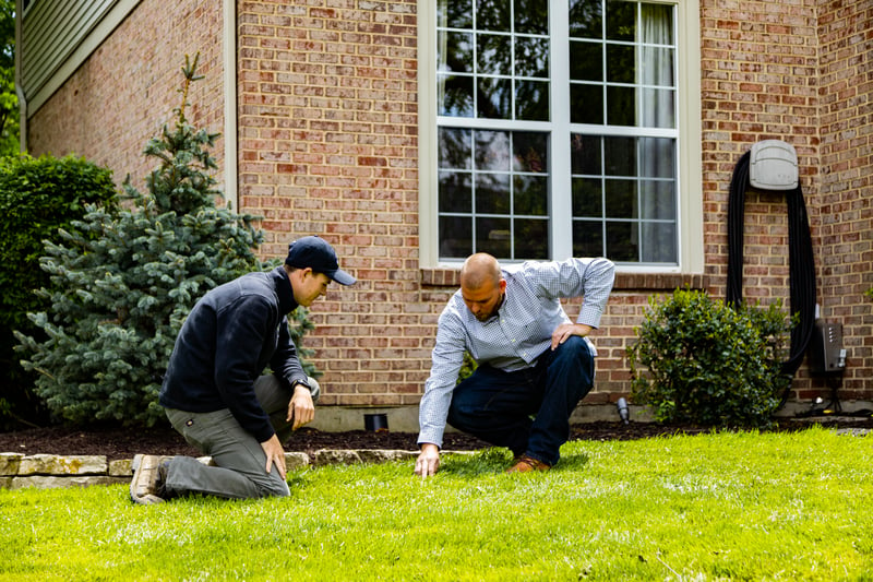 lawn care technician inspecting lawn with customer