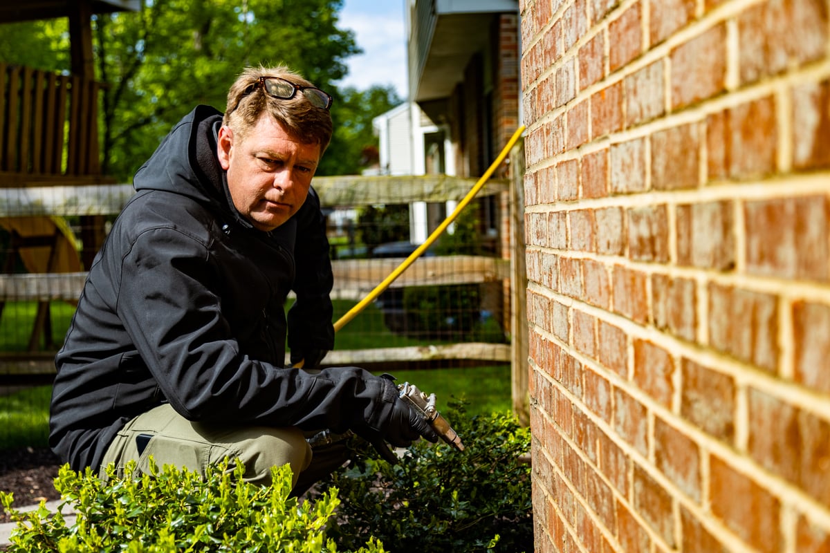 pest control technician sprays perimeter of home