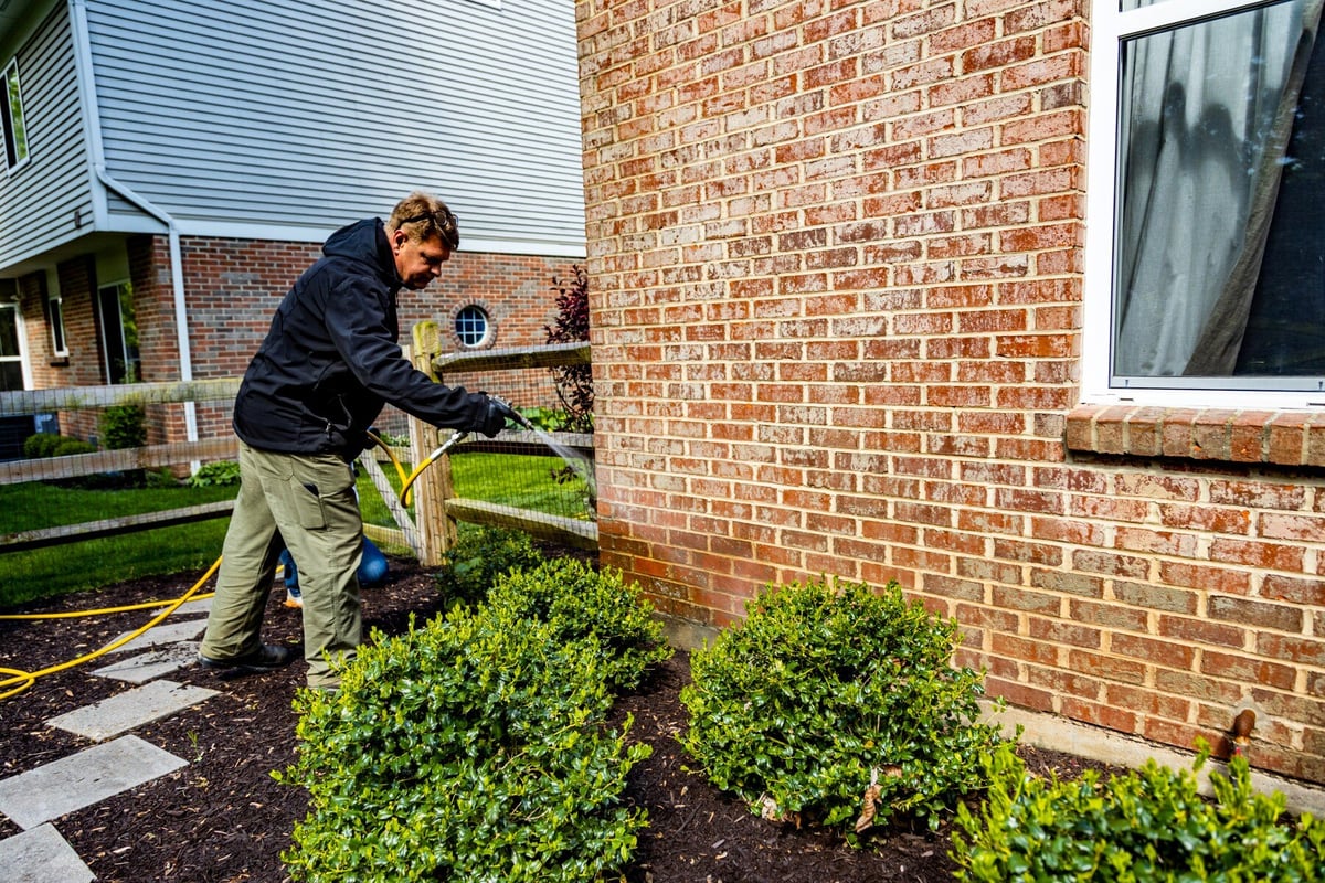 pest control expert sprays perimeter of home