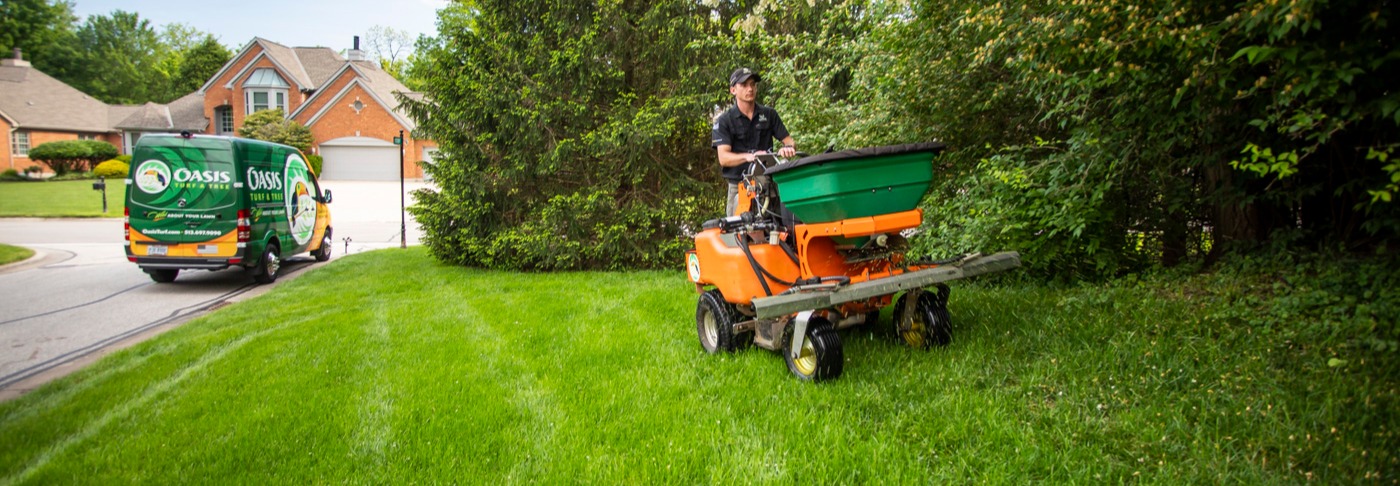 lawn care technician spreads grub control treatment with ride on sprayer