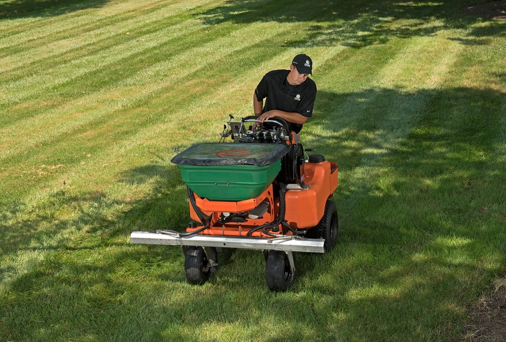 lawn care technician fertilizes grass