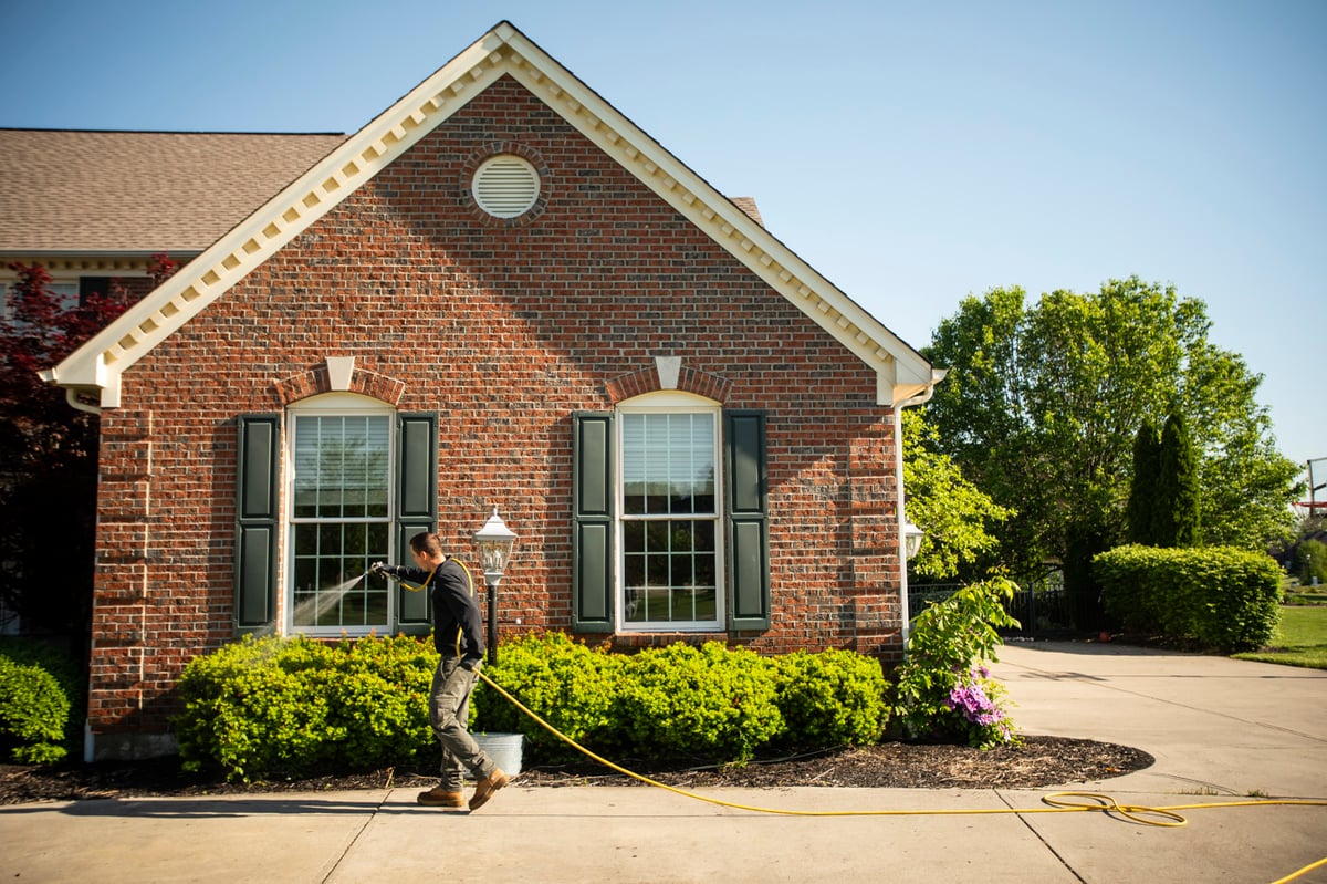 pest control technician sprays perimeter of home