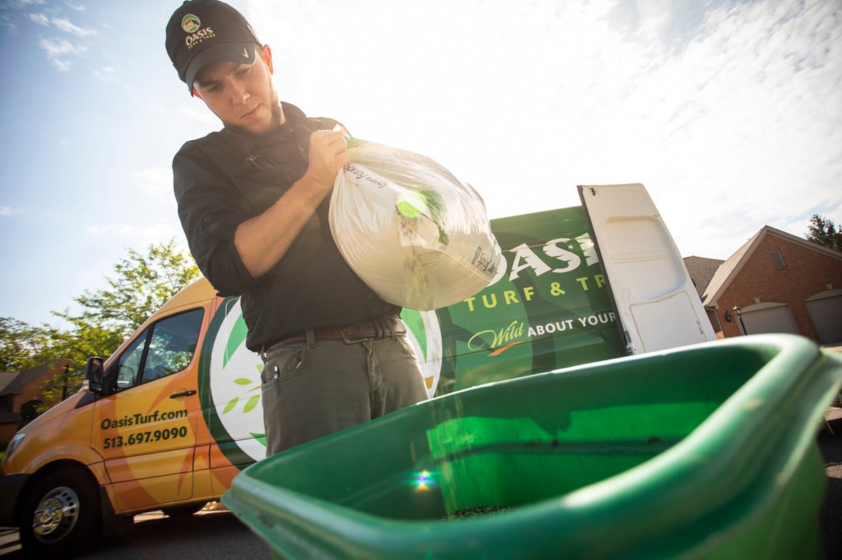 lawn care technician pours fertilizer into spreader