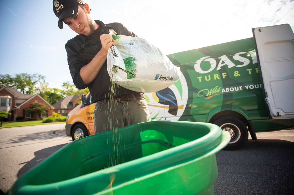 lawn care technician pours granular fertilizer into spreader