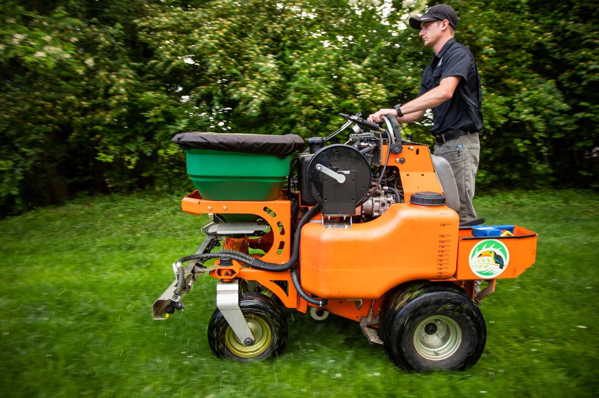 lawn care expert fertilizes grass with ride on spreader