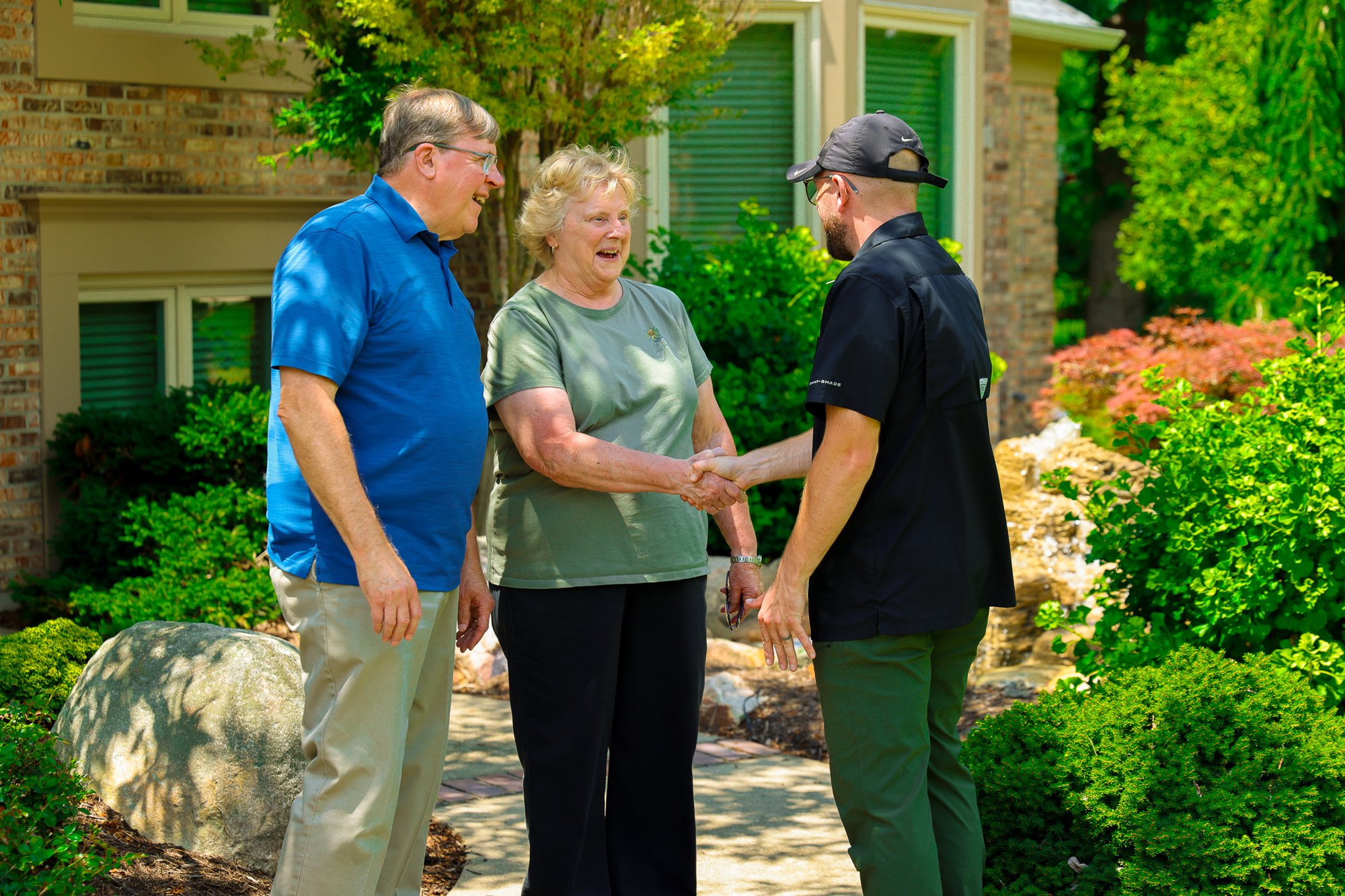 Man & woman smiling, happy shaking hands with oasis turf and tree employee