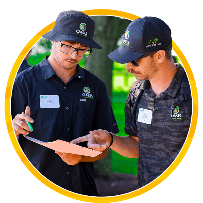 Two Oasis workers in branded hats and shirts review a paper outdoors, pointing to details in a collaborative moment framed by yellow.